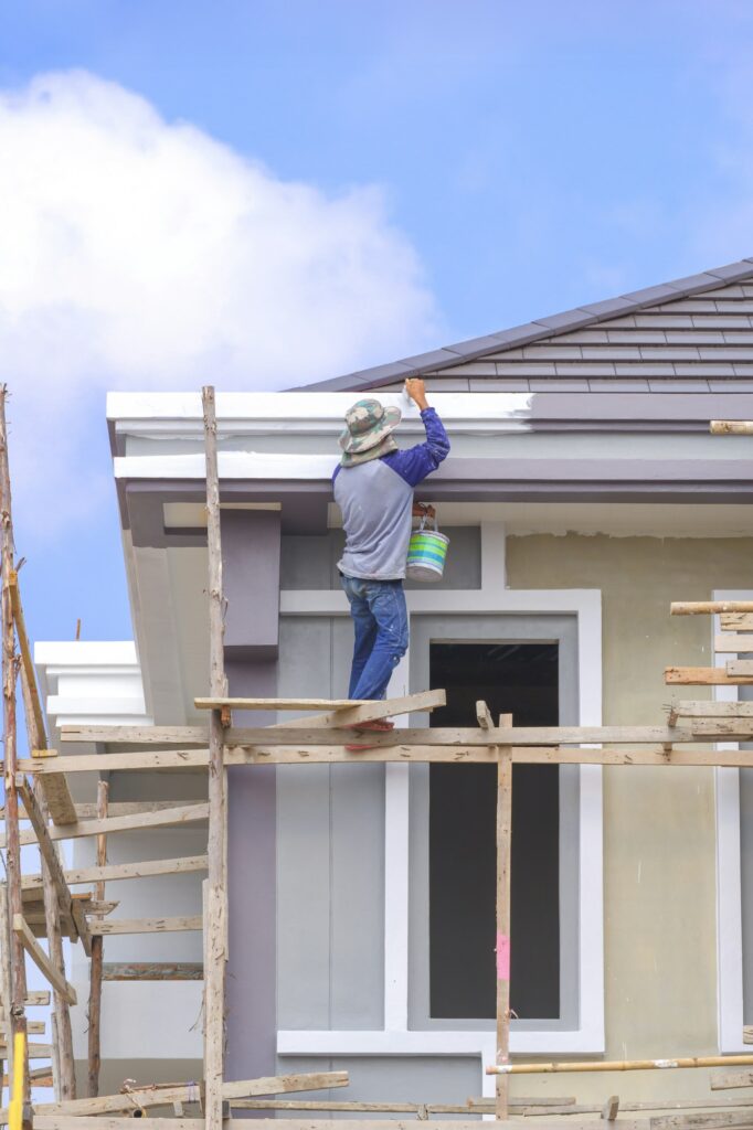 Painter on wooden scaffolding is painting roof eaves of modern house structure in construction site